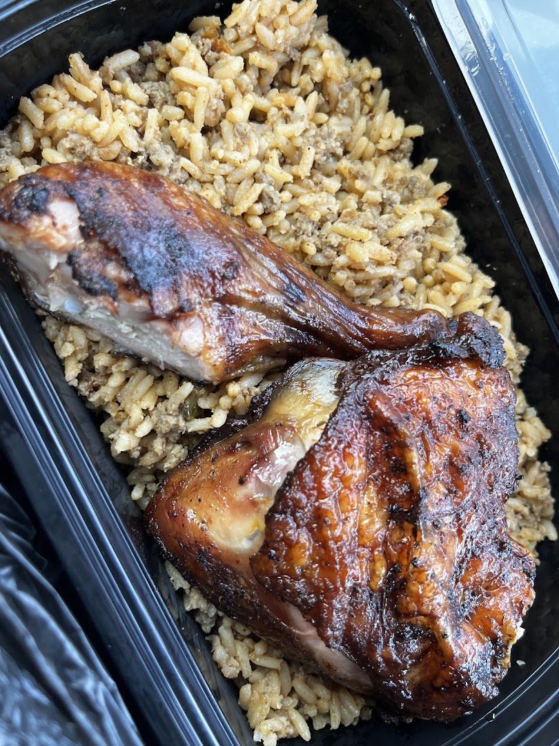 Smoked chicken quarters sitting on a bed of dirty rice in a black takeout container