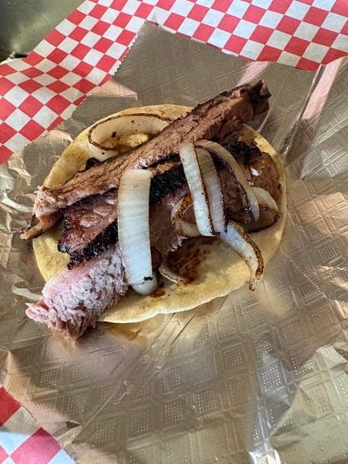 Open brisket taco topped with grilled onions on a soft tortilla