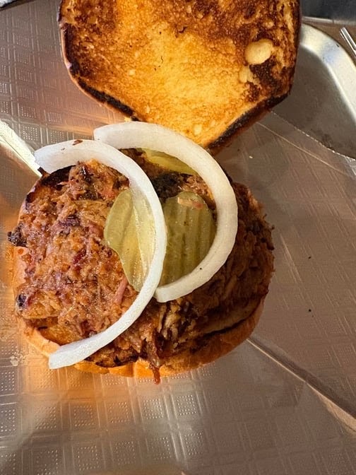 Open-faced chopped beef sandwich topped with pickle slices and raw onion