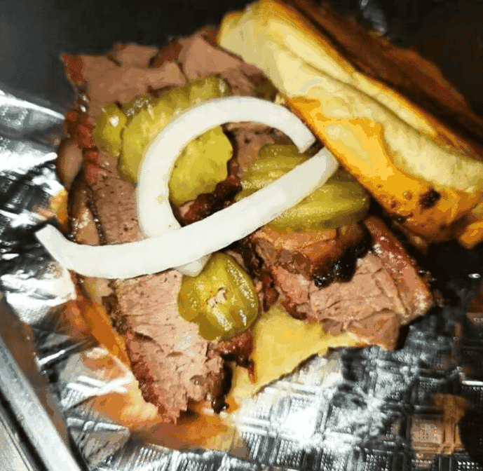 Brisket sandwich with pickles and onions sitting in a foil wrapper